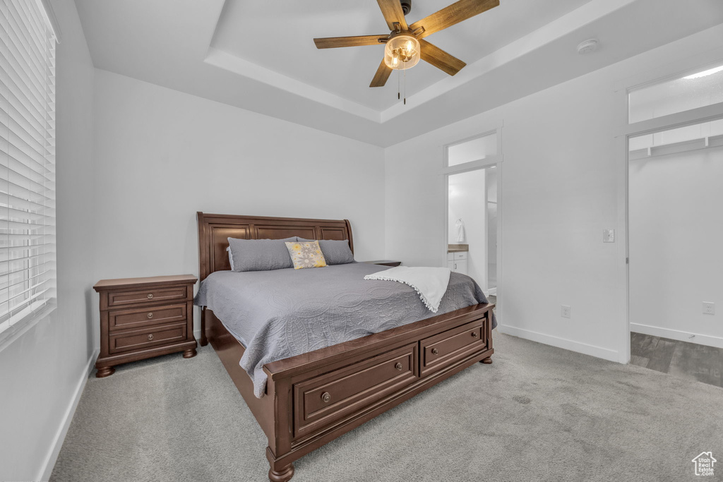 Carpeted bedroom featuring a raised ceiling, ensuite bathroom, a walk in closet, and ceiling fan