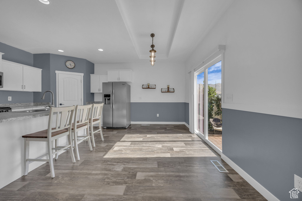Kitchen featuring stainless steel refrigerator with ice dispenser, white cabinets, a kitchen bar, wood finished floors, and recessed lighting