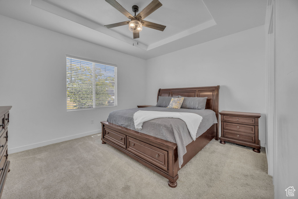 Bedroom with a raised ceiling, light colored carpet, and ceiling fan