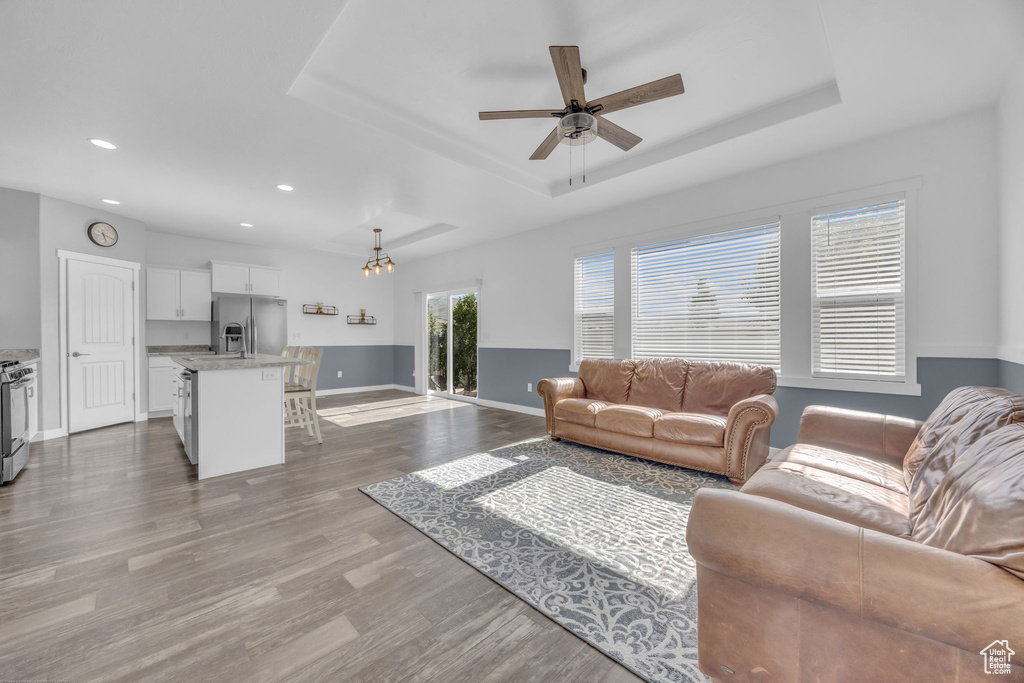 Living room with a tray ceiling, wood finished floors, ceiling fan, and recessed lighting