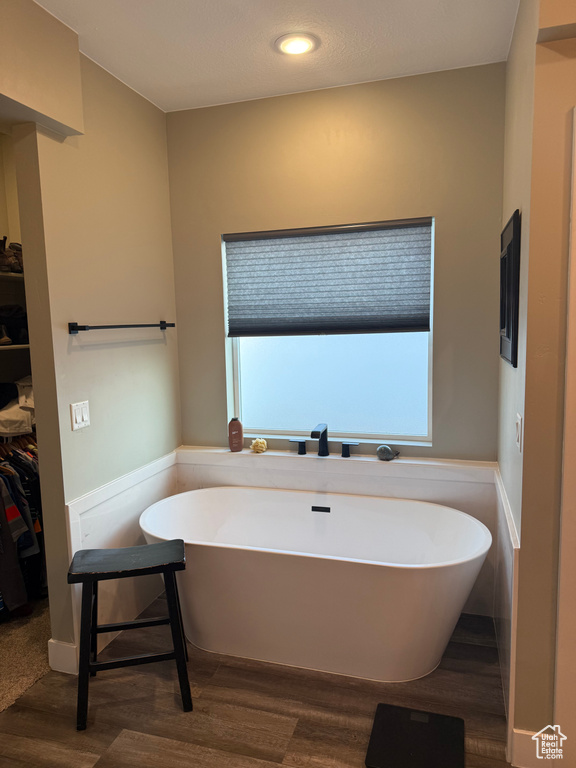 Full bath featuring wood finished floors, a freestanding tub, a walk in closet, and recessed lighting