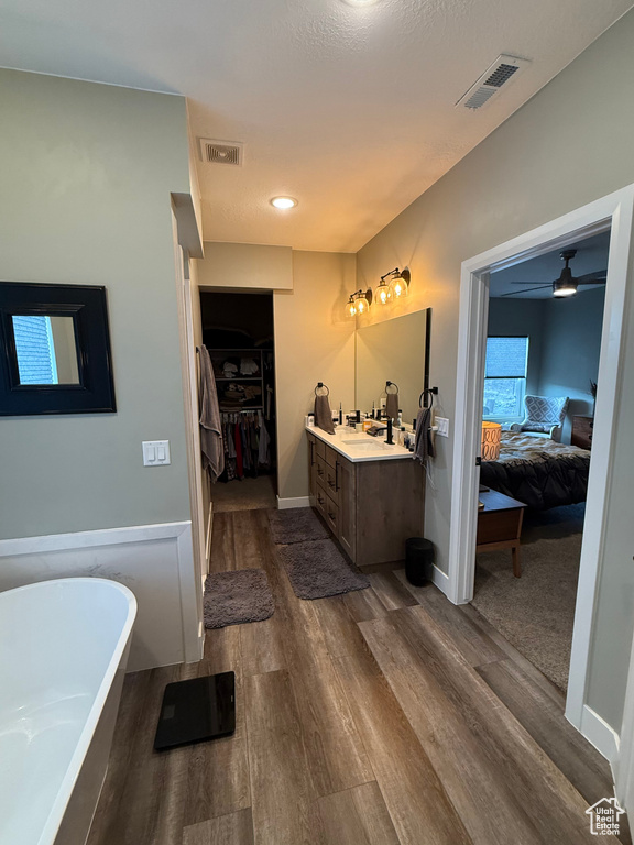 Bathroom featuring ensuite bathroom, a freestanding bath, vanity, wood finished floors, and a walk in closet