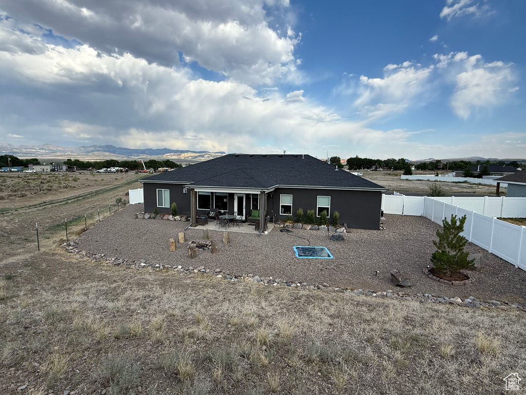 Rear view of house featuring a patio area, a mountain view, a fenced backyard, and a shingled roof