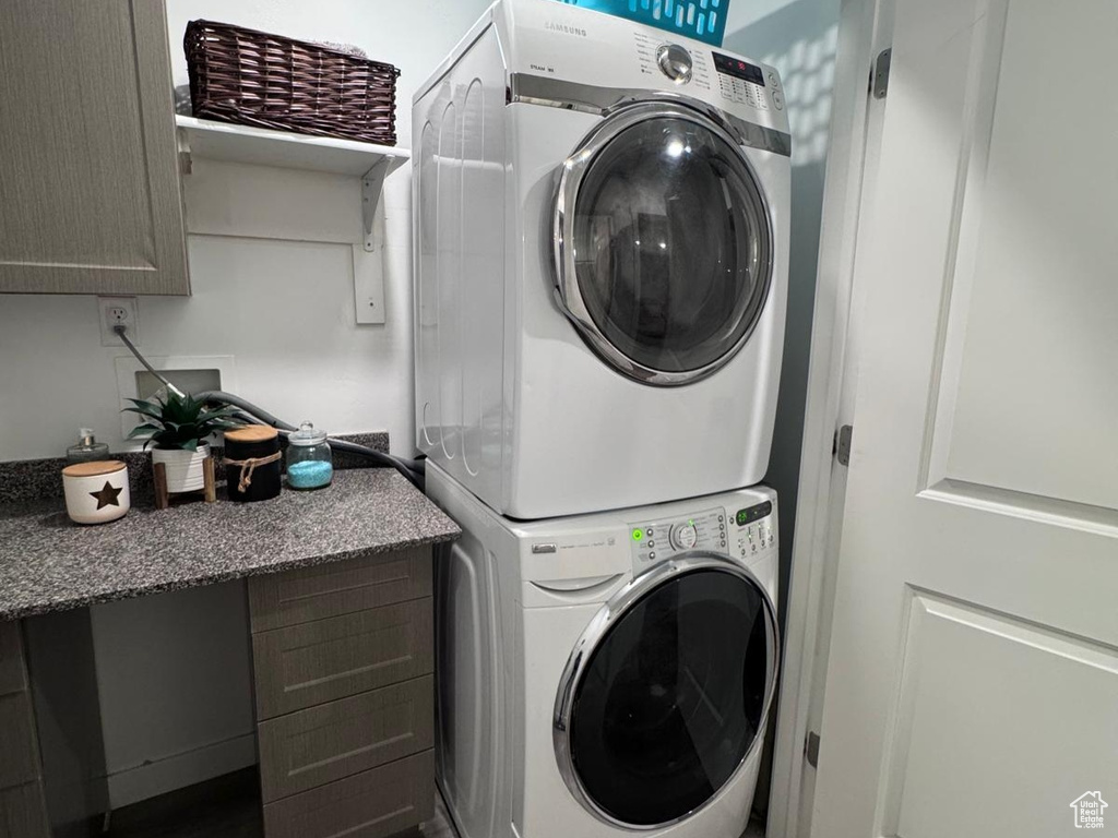 Laundry area featuring stacked washer / drying machine, light wood-style floors, and cabinet space
