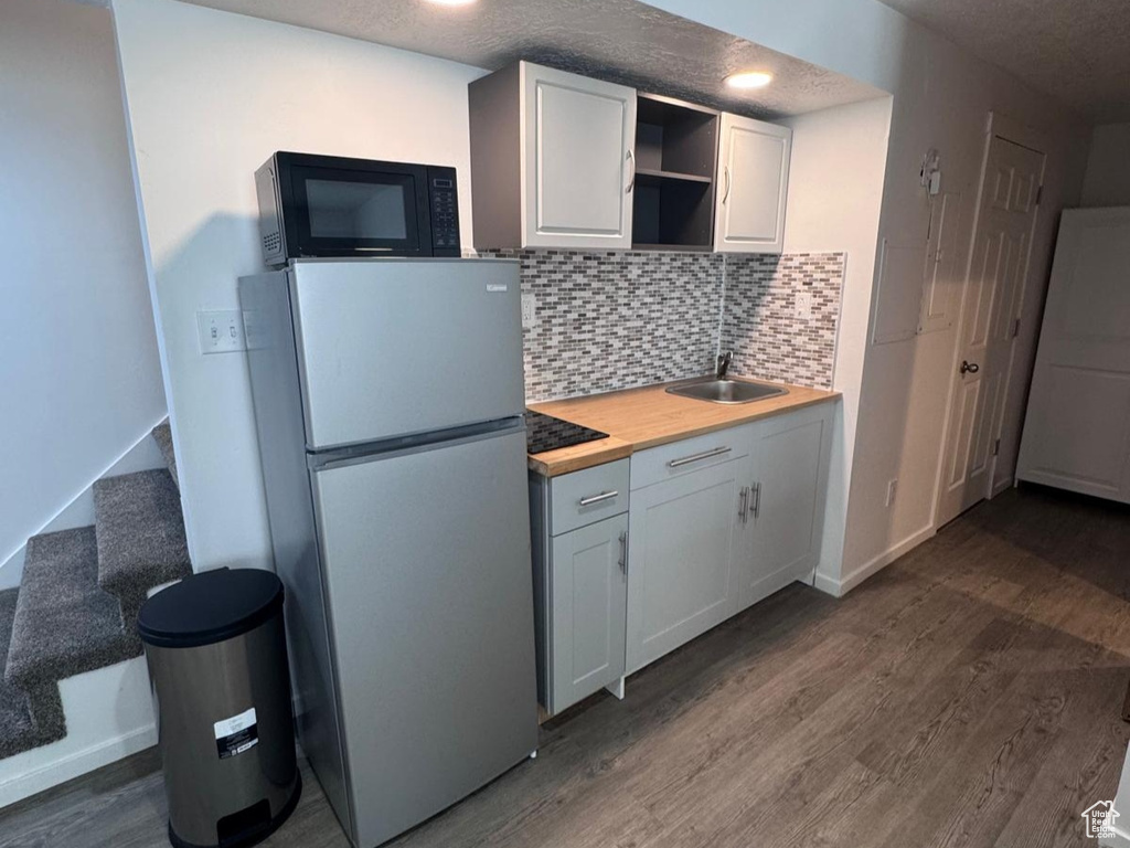 Kitchen featuring freestanding refrigerator, dark wood-style flooring, a textured ceiling, open shelves, and backsplash