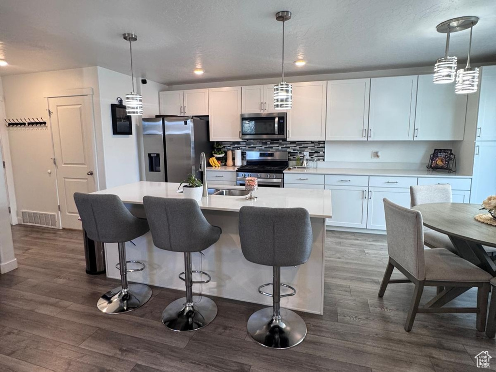 Kitchen featuring stainless steel appliances, a kitchen island with sink, white cabinetry, light countertops, and a textured ceiling