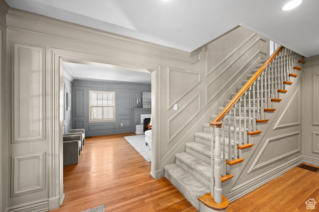 Stairway with a decorative wall, crown molding, wood finished floors, and a warm lit fireplace