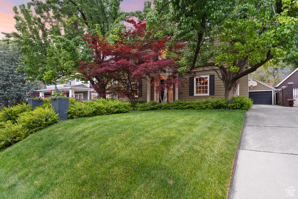 View of property hidden behind natural elements with a front yard, an outbuilding, and a garage