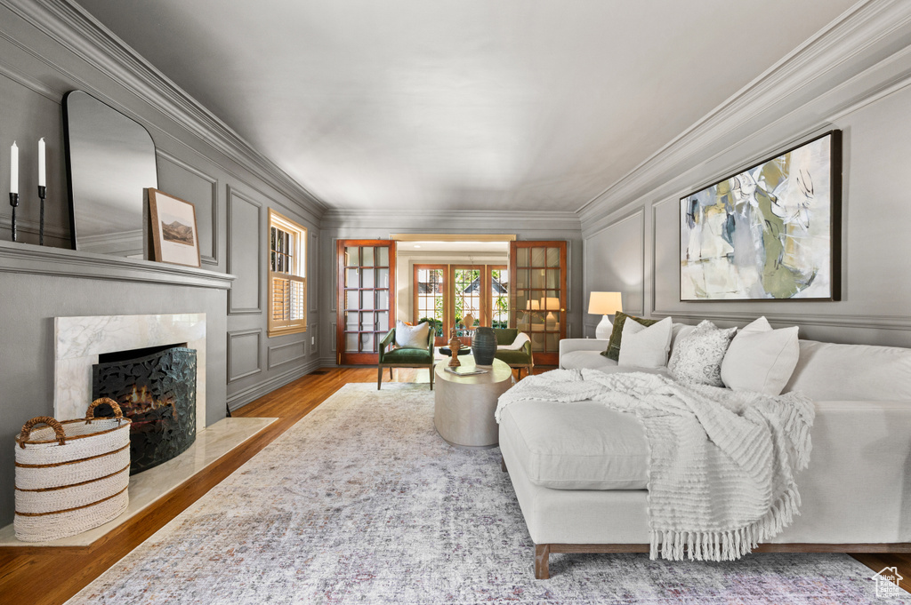 Bedroom with crown molding, a decorative wall, wood finished floors, a fireplace, and french doors