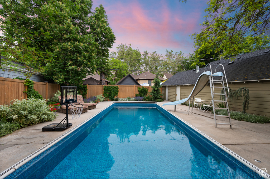 View of swimming pool with a patio, a fenced backyard, a water slide, and a shed