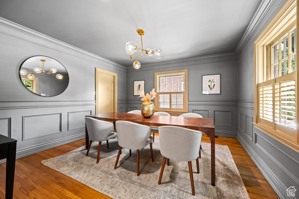 Dining area featuring a chandelier, dark wood finished floors, ornamental molding, a decorative wall, and wainscoting