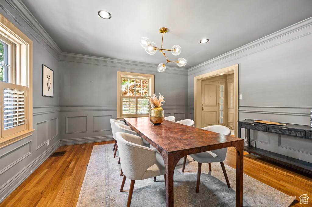 Dining area with a decorative wall, ornamental molding, light wood-style flooring, a chandelier, and recessed lighting
