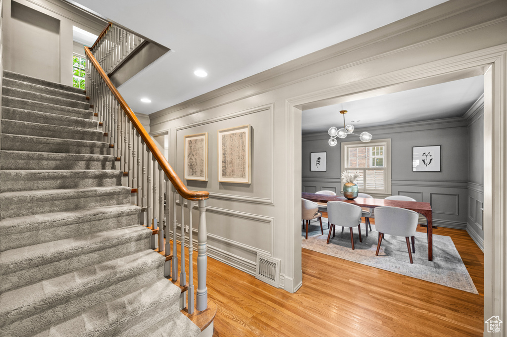 Stairway featuring a decorative wall, crown molding, wood finished floors, healthy amount of natural light, and a chandelier