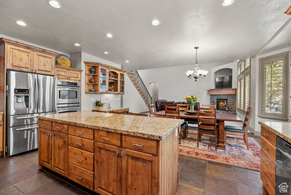 Kitchen with stainless steel appliances, a center island, recessed lighting, light stone countertops, and open shelves
