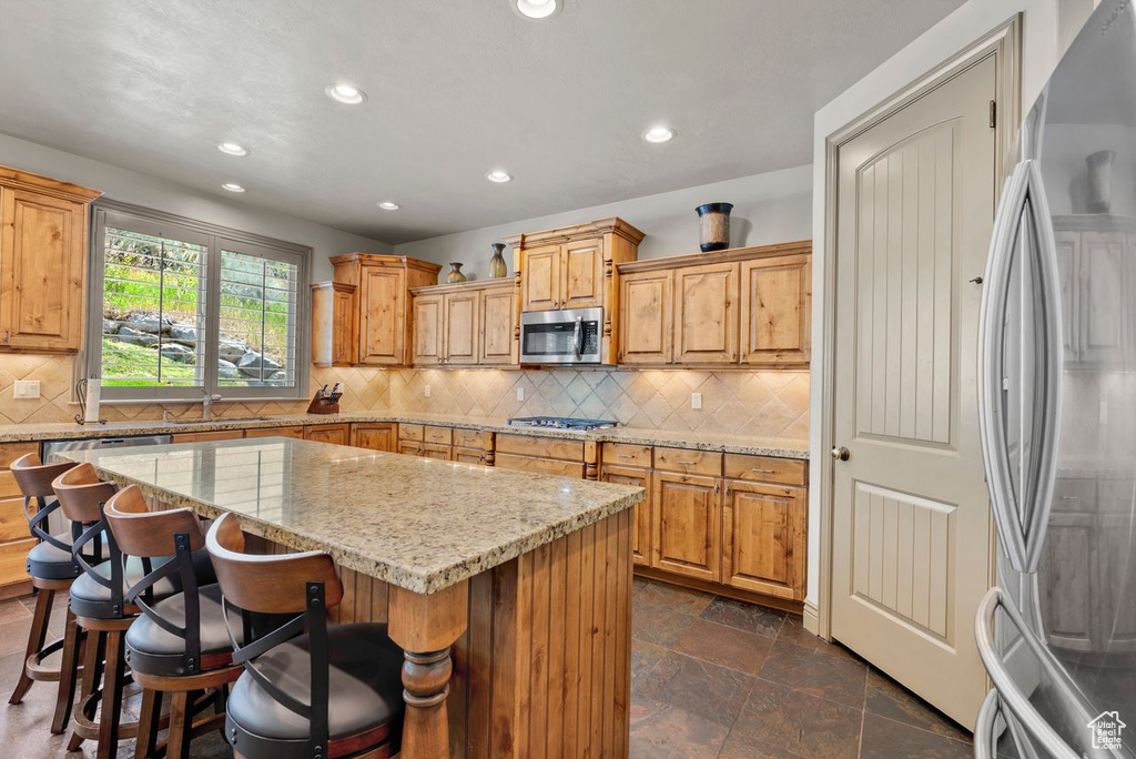 Kitchen with stainless steel appliances, recessed lighting, a center island, a kitchen breakfast bar, and light stone counters