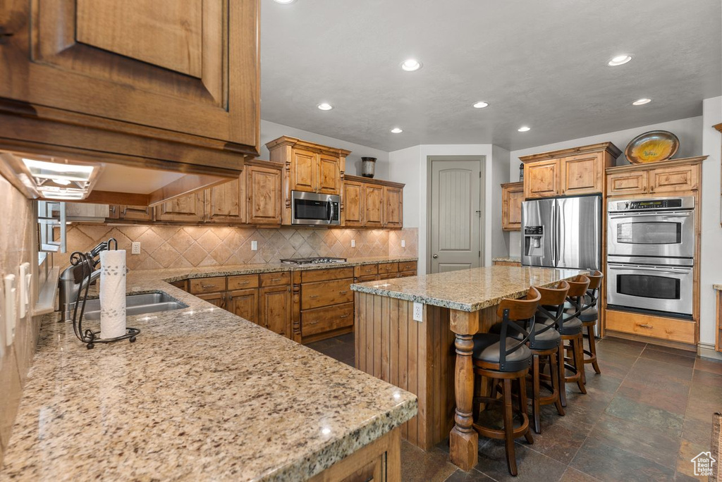 Kitchen with appliances with stainless steel finishes, recessed lighting, light stone counters, brown cabinets, and a center island