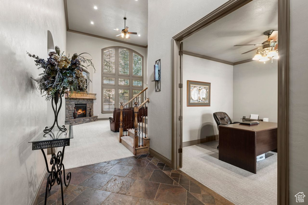 Entryway with a ceiling fan, stone tile flooring, ornamental molding, a stone fireplace, and stairs