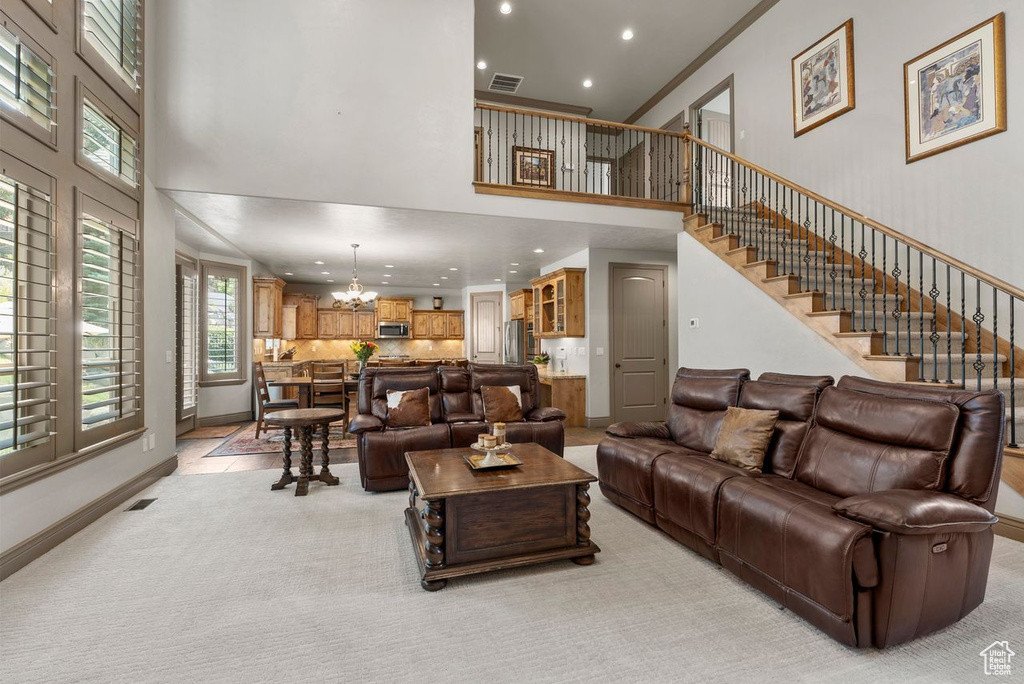 Living room with a towering ceiling, recessed lighting, a chandelier, light colored carpet, and stairs