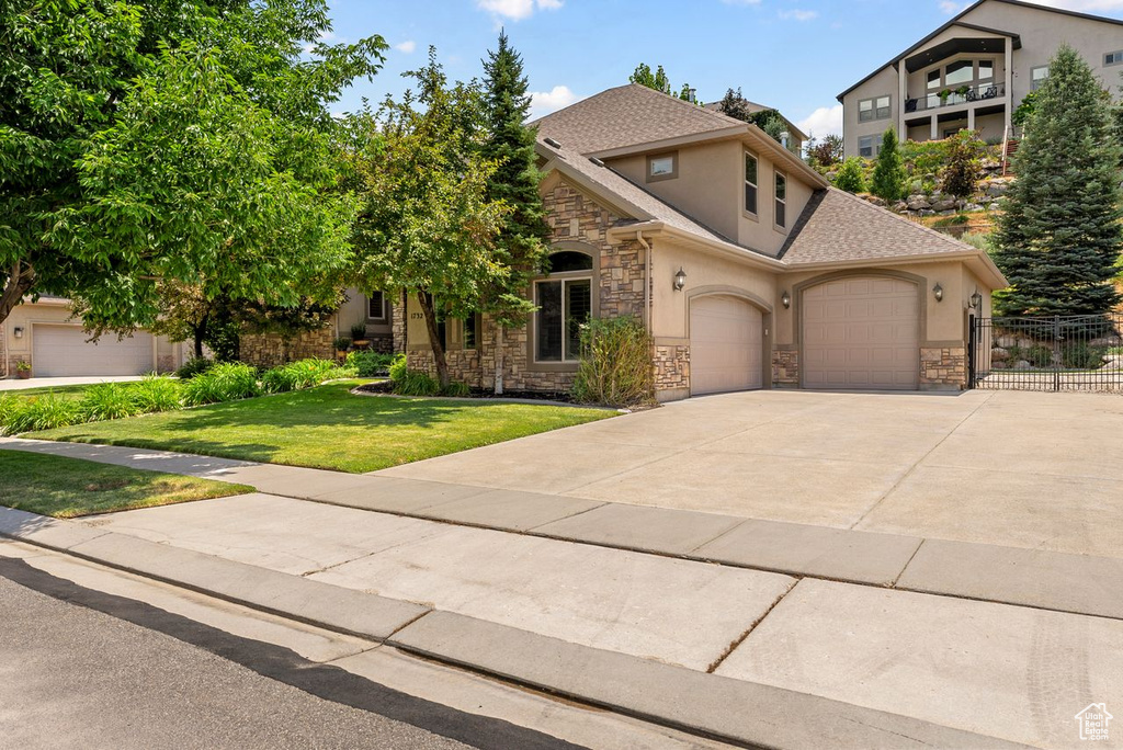 View of front facade with stucco siding, driveway, stone siding, roof with shingles, and a garage