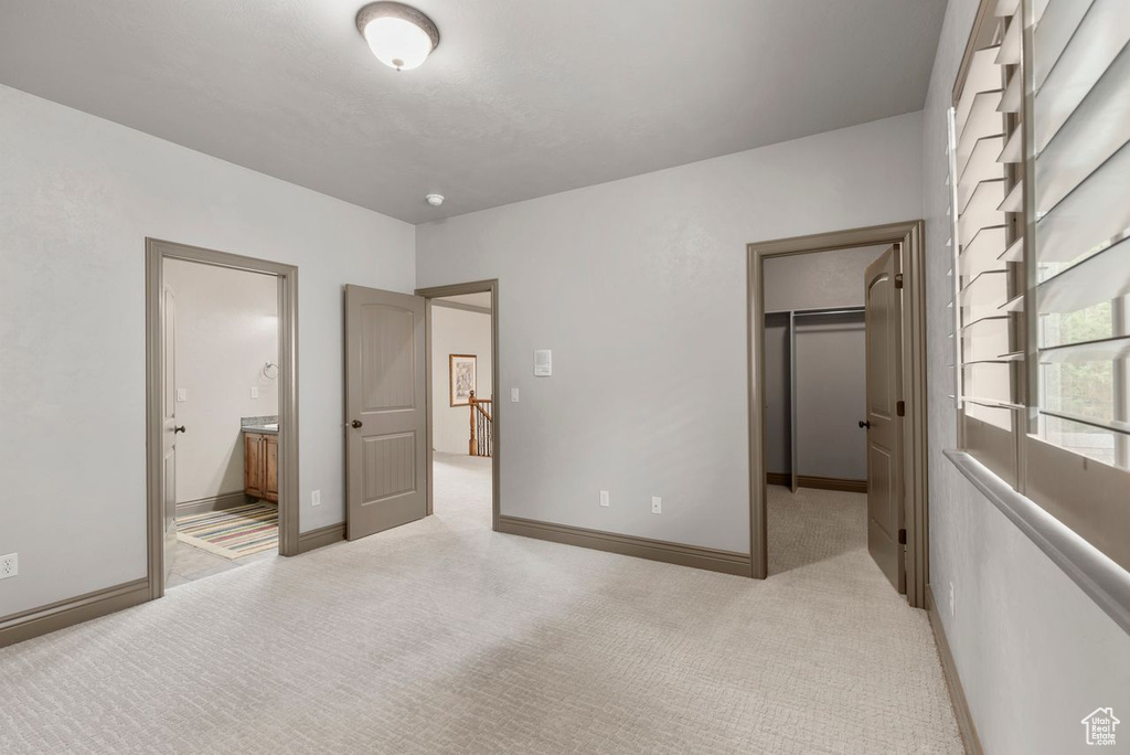 Unfurnished bedroom featuring a walk in closet, light colored carpet, and connected bathroom