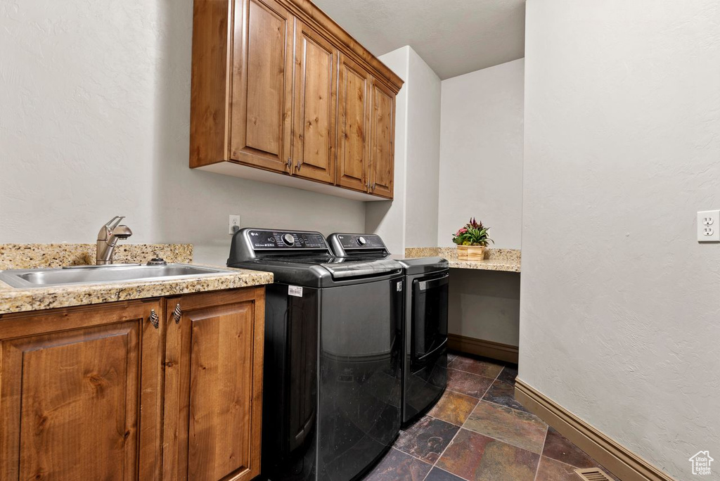 Washroom with washing machine and clothes dryer, cabinet space, and dark stone finish floors