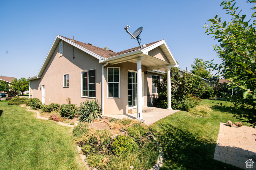Back of house featuring stucco siding, a patio area, and a lawn
