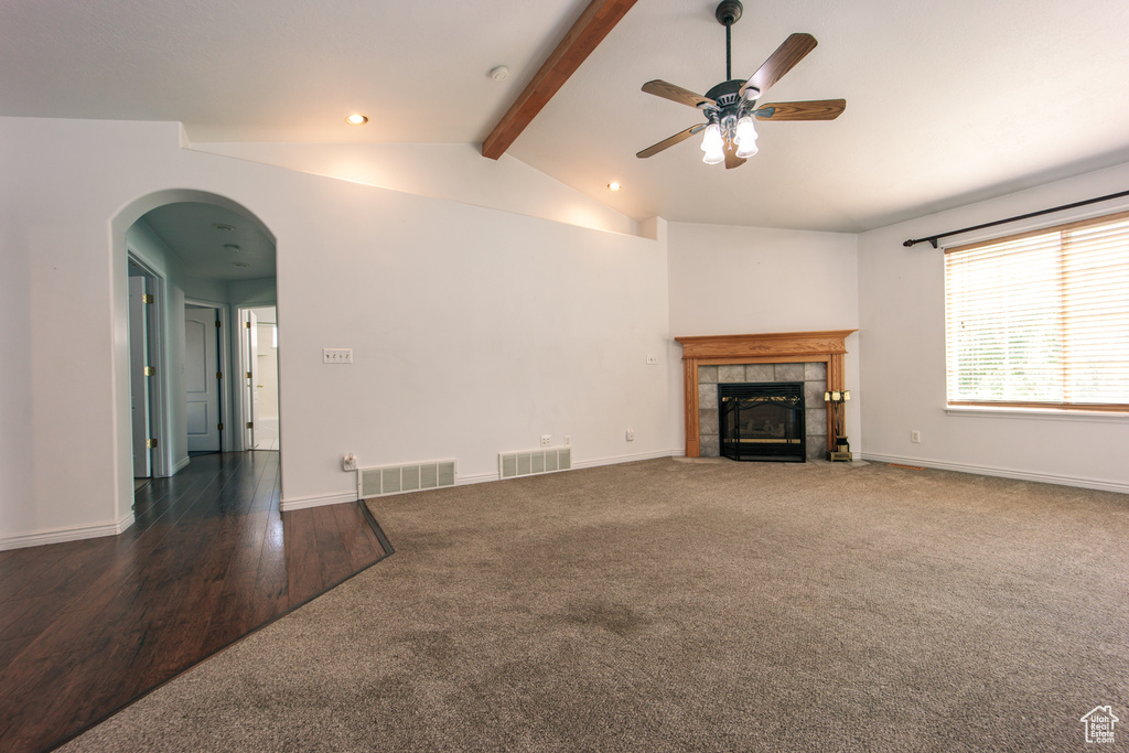 Unfurnished living room featuring a tile fireplace, carpet flooring, ceiling fan, arched walkways, and wood finished floors