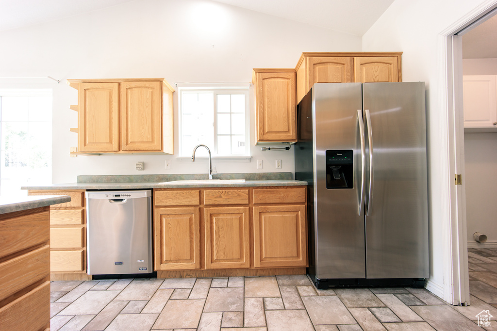 Kitchen with appliances with stainless steel finishes, light brown cabinets, vaulted ceiling, and light stone finish floors