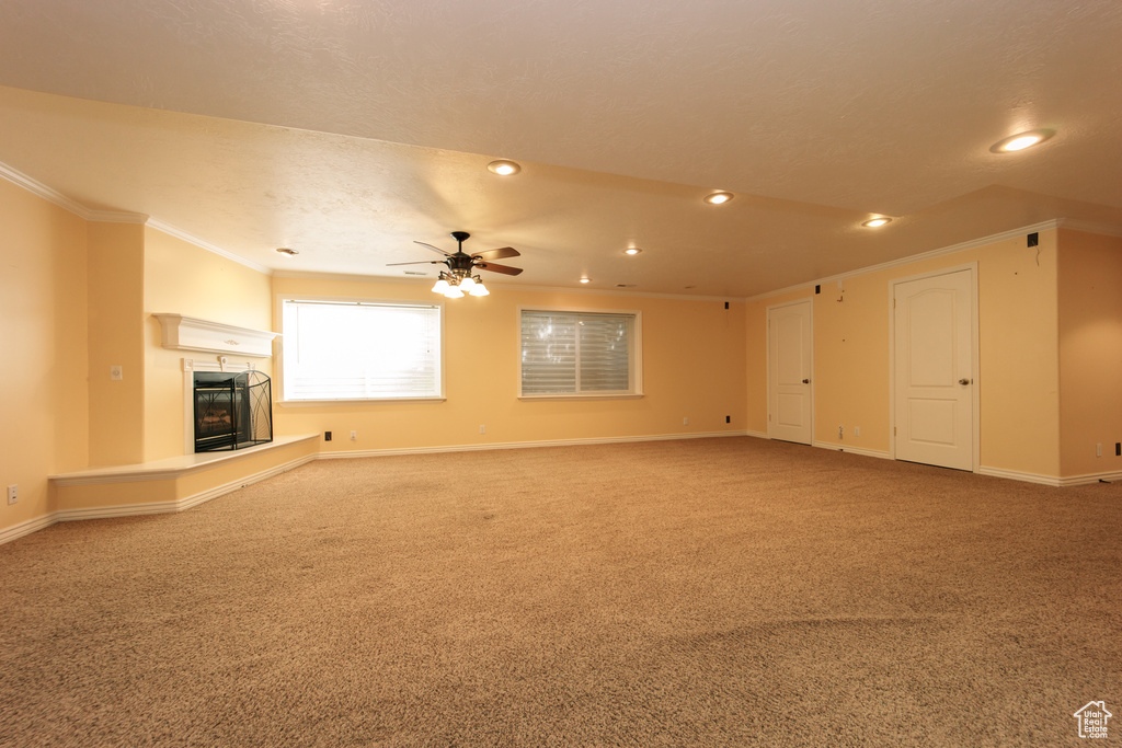 Unfurnished living room featuring crown molding, a glass covered fireplace, carpet floors, recessed lighting, and a ceiling fan