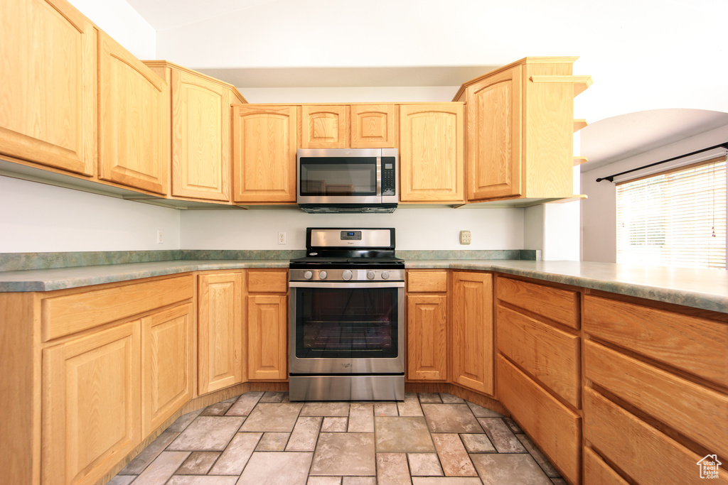 Kitchen featuring appliances with stainless steel finishes, light brown cabinetry, and stone finish floors