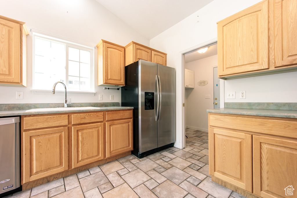 Kitchen featuring stainless steel appliances, light brown cabinetry, lofted ceiling, and stone finish flooring