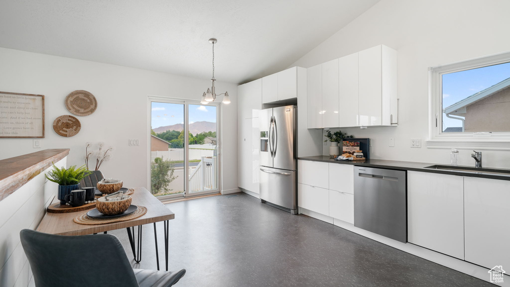 Kitchen featuring stainless steel appliances, white cabinetry, dark countertops, decorative light fixtures, and lofted ceiling