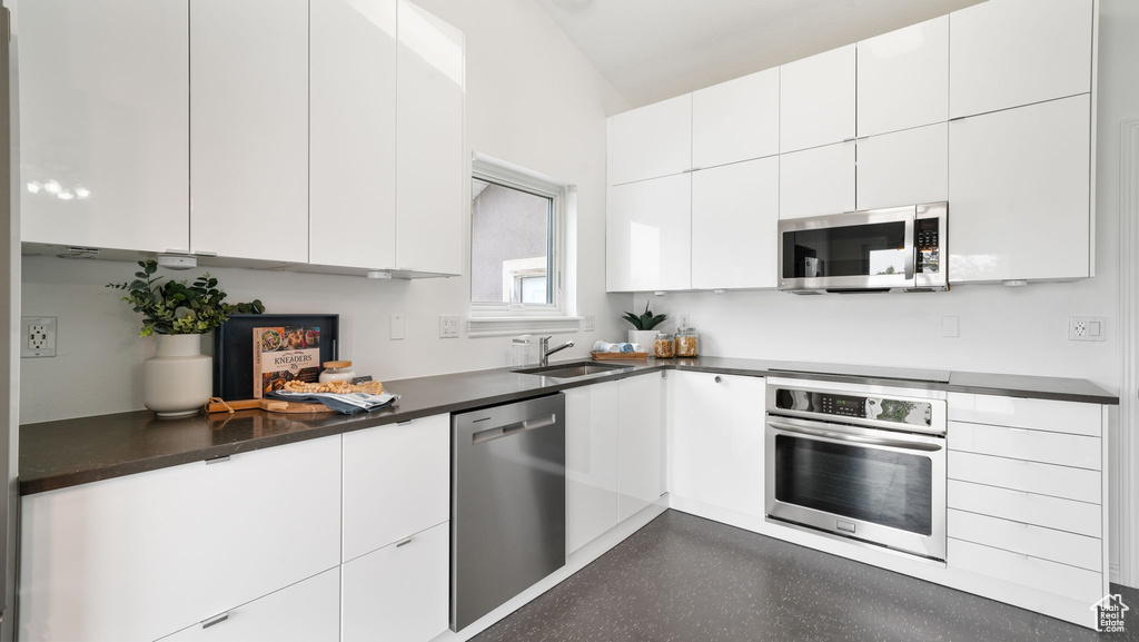Kitchen featuring appliances with stainless steel finishes, white cabinets, dark countertops, and vaulted ceiling