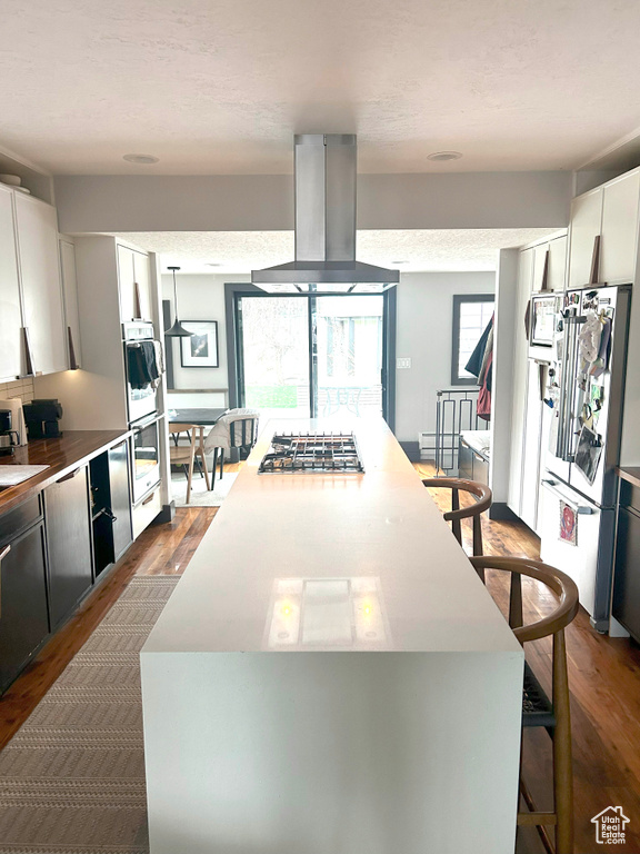Kitchen with dark wood finished floors, appliances with stainless steel finishes, extractor fan, a breakfast bar area, and white cabinets