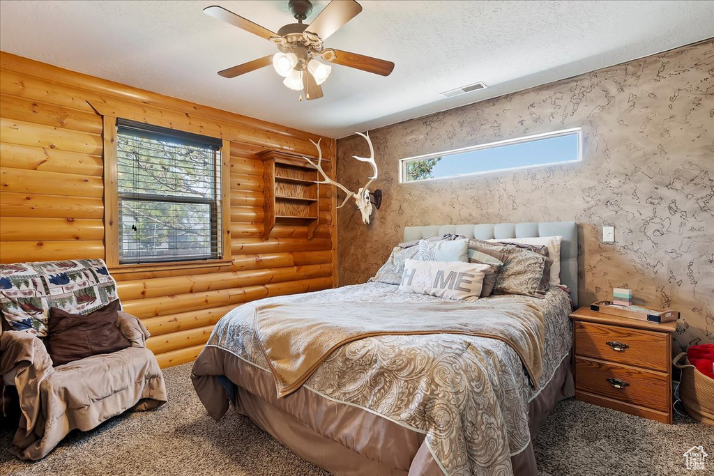 Carpeted bedroom with rustic walls and a ceiling fan