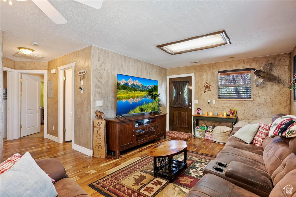 Living area with light wood-style floors, a textured ceiling, and a ceiling fan