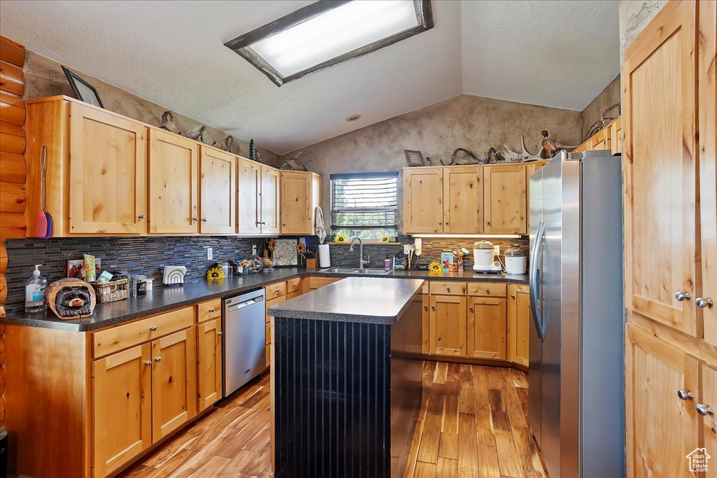 Kitchen with appliances with stainless steel finishes, light wood-style flooring, vaulted ceiling, dark countertops, and backsplash