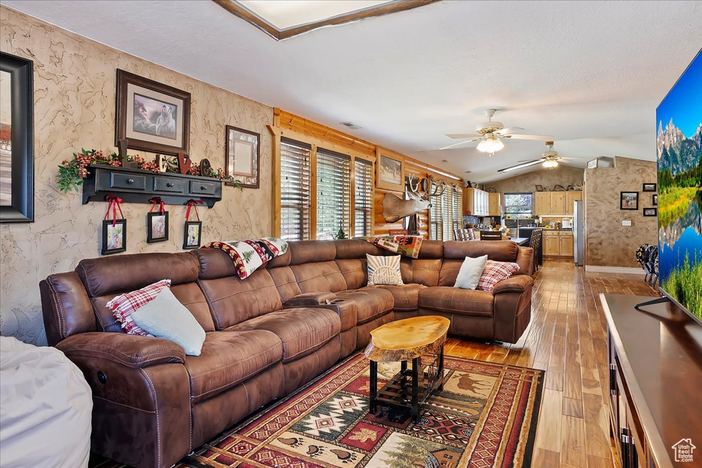 Living room featuring lofted ceiling, a ceiling fan, light wood-style floors, and wallpapered walls