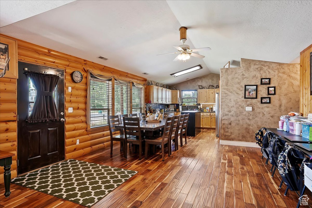 Dining area with a ceiling fan, light wood-type flooring, vaulted ceiling, log walls, and plenty of natural light