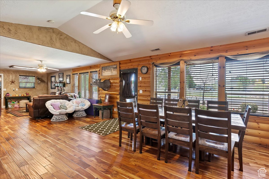 Dining space with ceiling fan, wood finished floors, vaulted ceiling, and rustic walls