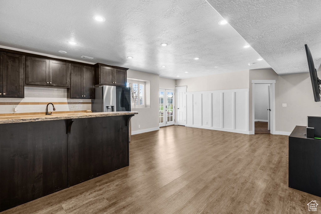 Kitchen featuring a textured ceiling, dark brown cabinets, recessed lighting, wood finished floors, and a breakfast bar