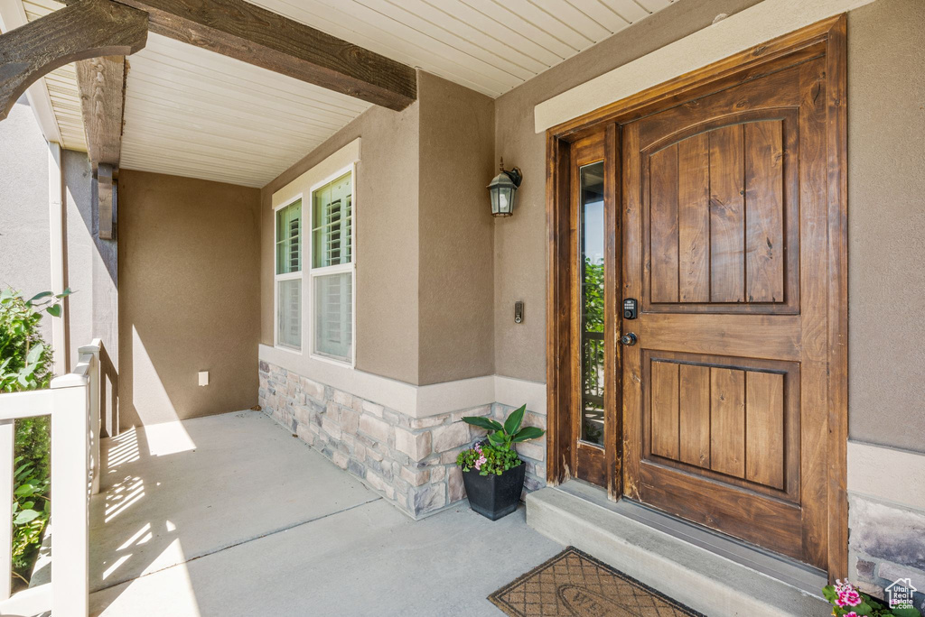 Doorway to property featuring covered porch, stone siding, and stucco siding