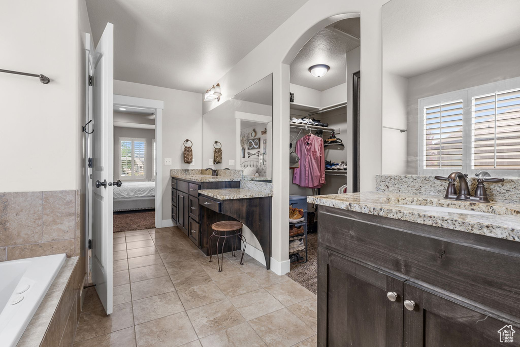 Full bathroom featuring vanity, ensuite bath, a relaxing tiled tub, a walk in closet, and tile patterned flooring