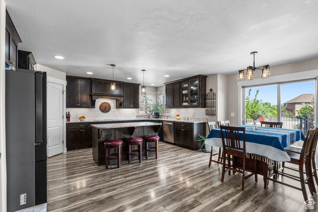 Kitchen with healthy amount of natural light, wood finished floors, a kitchen island, dark brown cabinets, and a textured ceiling