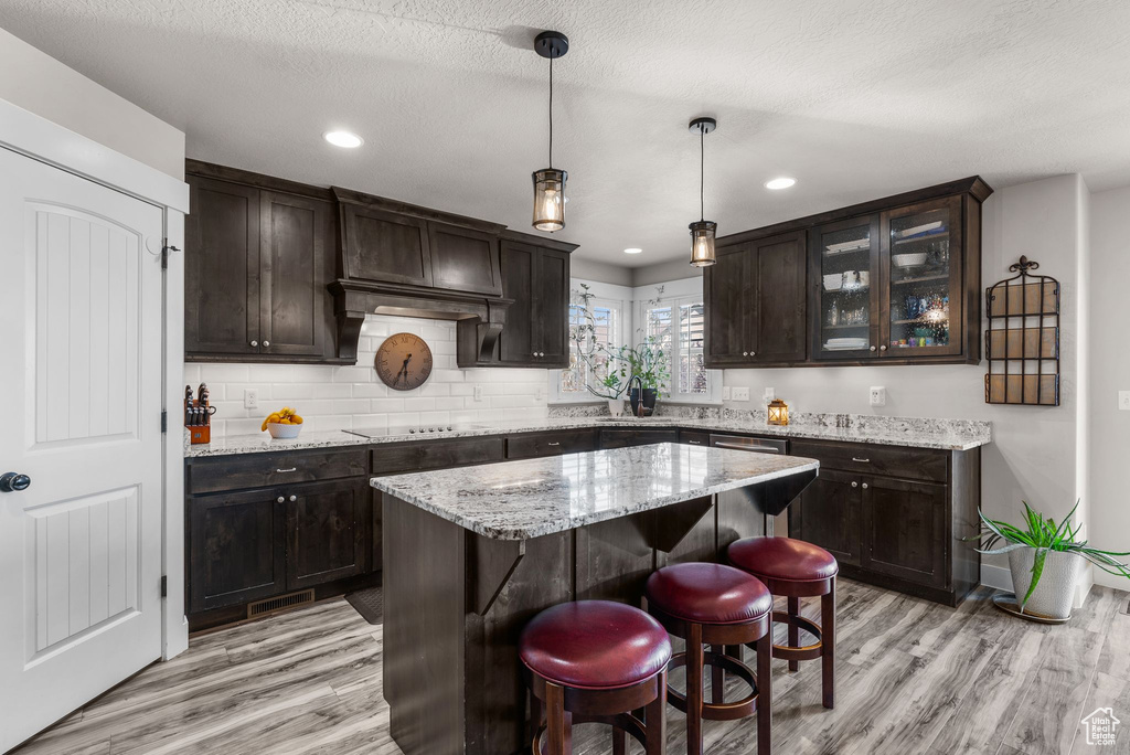 Kitchen featuring light wood finished floors, dark brown cabinetry, recessed lighting, pendant lighting, and light stone countertops