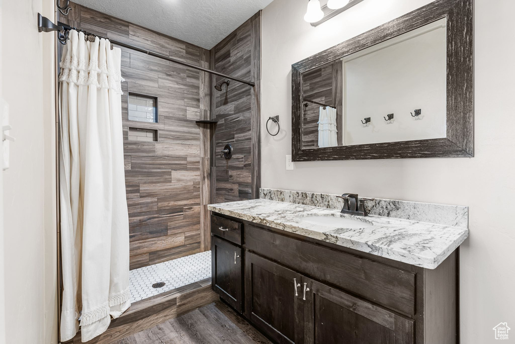Full bath with vanity, a tile shower, and wood finished floors