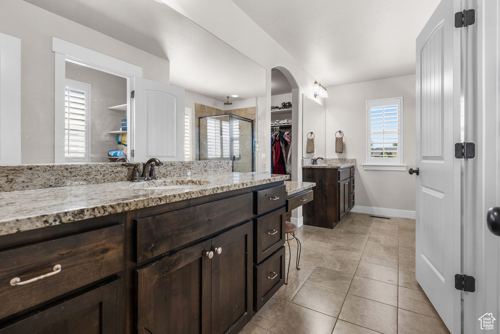 Full bath featuring a stall shower, a spacious closet, two vanities, and plenty of natural light