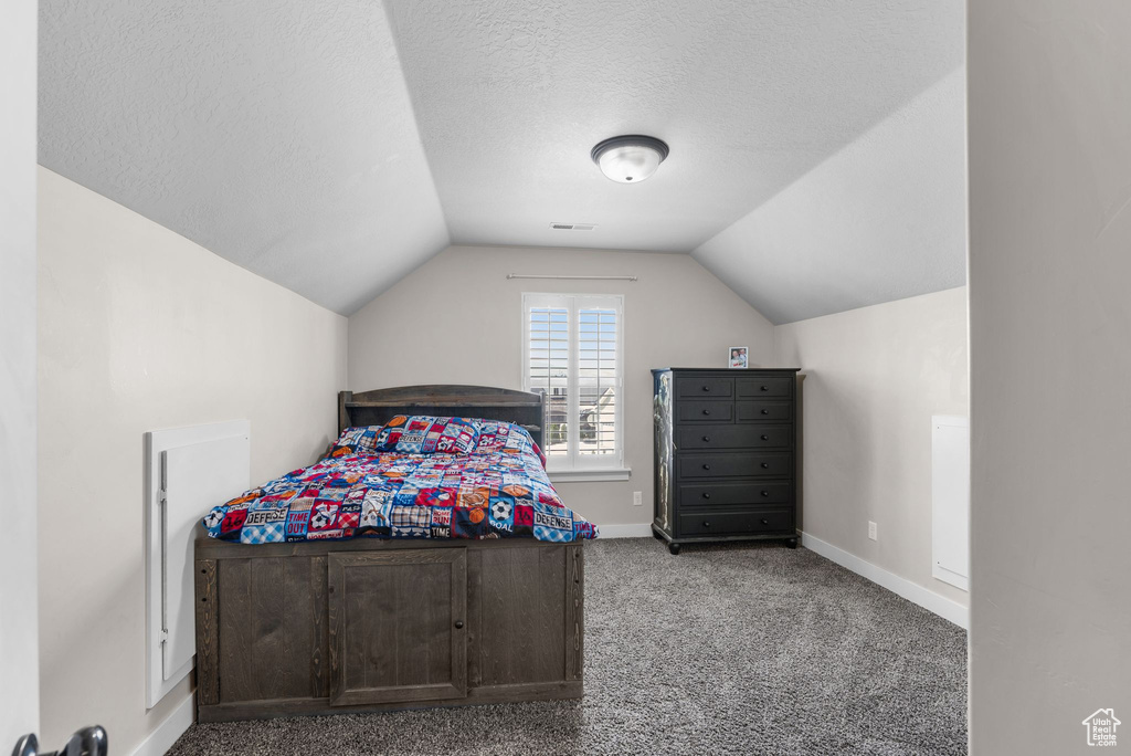 Bedroom with vaulted ceiling, carpet, and a textured ceiling