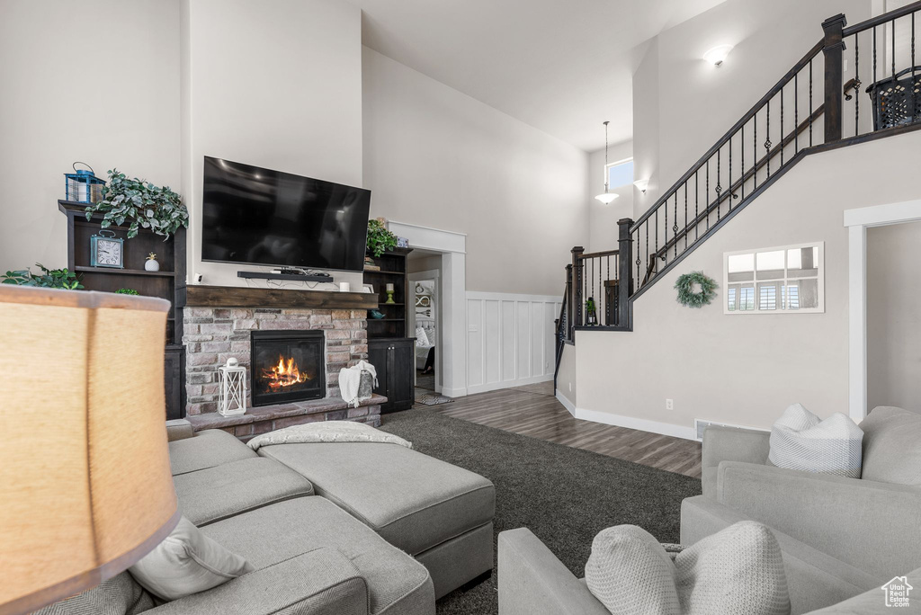 Living area featuring a towering ceiling, stairway, wood finished floors, and a stone fireplace
