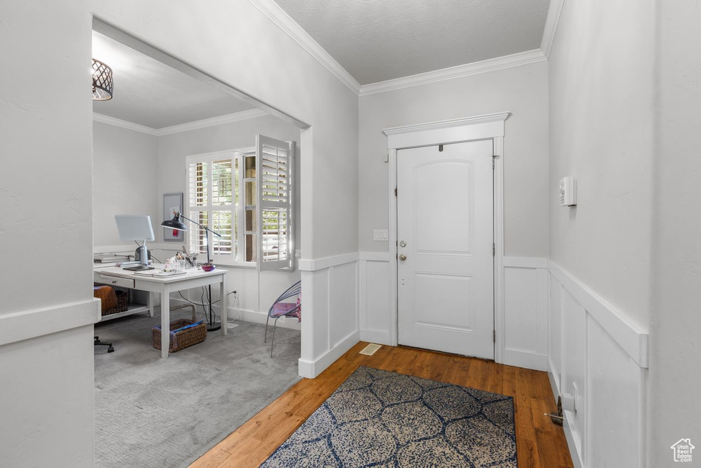 Foyer with wood-type flooring, ornamental molding, and a wainscoted wall